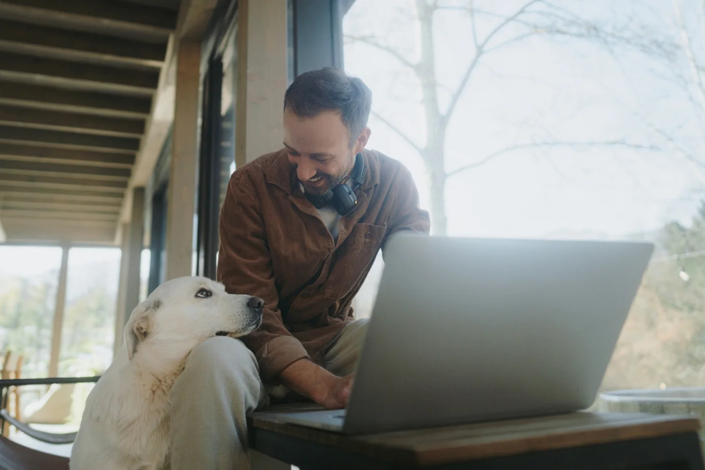 Person working remotely from home with a laptop and dog nearby, representing flexible work environments and the need for secure, easy file access from any location.